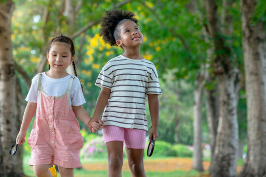 Two little girls of different skin colors hold hands and take a walk in the park on a beautiful summer day, Diverse friends