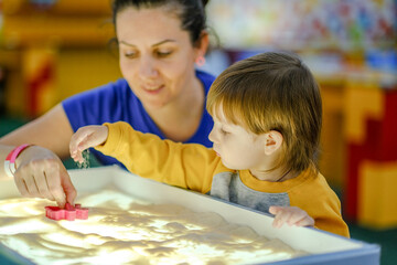 Creative early baby development. A mother teaches her child to draw with her fingers in the sand. Center for the Development of Children with Autism.