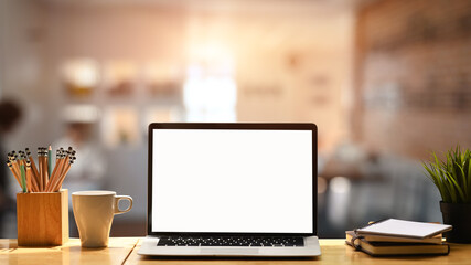 Naklejka premium Front view mock up laptop computer, coffee cup, pencil holder, notebook and houseplant on wooden table.