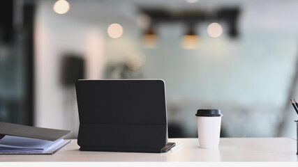 Computer tablet, cup of coffee and paperworks on white office desk.