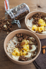 Oatmeal with pineapple, banana and chocolate granola in beige plates on a brown wooden table. A hearty healthy breakfast. Selective focus