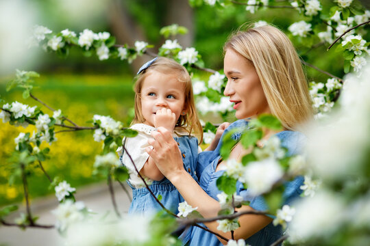 Happy mother's day. Little girl hugs her mother in the spring cherry garden. Portrait of happy mother and daughter among white flowers trees. Family values. Motherhood. Mom and child in blooming park