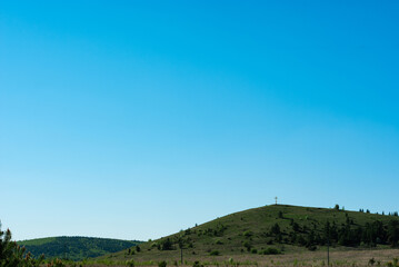 Rolling hills in summer with christian cross on the top of one and very clean blue sky