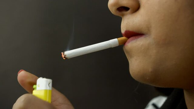 Closeup shot - An Indian female lighting up a toxic cigarette and smoking. Side view shot of an addicted young girl puffing a cigarette and exhaling smoke - unhealthy lifestyle 