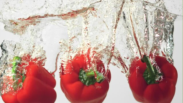 Super slow motion red pepper falls under the water with splashes. On a white background. Filmed on a high-speed camera at 1000 fps.