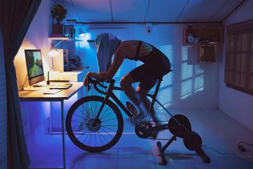 Foto op Plexiglas Asian man cyclist. She is exercising in the house.By cycling on the trainer and play online bike games.. © torwaiphoto