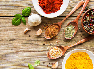 A selection of various colorful spices on a wooden table in bowls and spoons