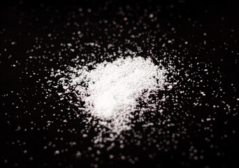 A close-up select focus picture of a pile some of white salt is a salty culinary ingredient mixed with spices, cooking on a black background.