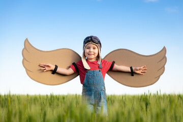 Happy child with cardboard wings playing outdoor in summer