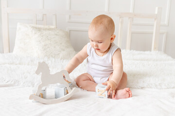 baby plays with wooden toys cubes on the bed in a bright room