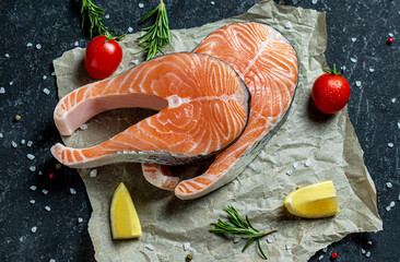Two fresh raw salmon steaks with salt, peppers, lemon, tomatoes and rosemary on the rustic paper