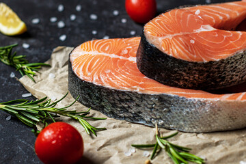 Fresh raw salmon steaks with salt, peppers, lemon, tomatoes and rosemary on the rustic paper