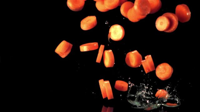 Super slow motion pieces of carrot fall into the water with splashes. On a black background. Filmed on a high-speed camera at 1000 fps. High quality FullHD footage