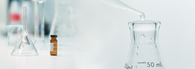 drop of water into flask with drug vial and glassware in medical science lab banner background