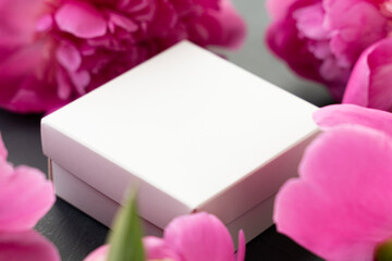 Small white box in a frame of pink delicate peonies on a beautiful cement background . Romantic concept. Flat lay.Postcard