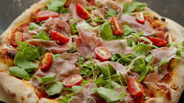Delicious Pizza with prosciutto parma ham, arugula salad rocket and cherry tomato on rusty dark