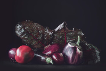 vegetables on a dark background, red and purple colors, eggplant, peppers and onions, fresh plant foliage, studio shot.
