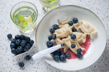 Curd dumplings or vareniki with fresh bilberry, elevated view on a beige stone background, horizontal shot