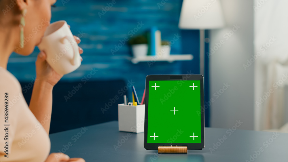 Poster woman drinking a cup of coffee while looking at tablet computer with mock up green screen chroma key