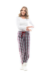Happy confident pretty young woman in cozy pajama showing and presenting copy space. Full body length isolated on white background.