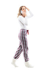 Side view of happy young woman in pajama talk on the phone walking looking up. Full body length isolated on white background.