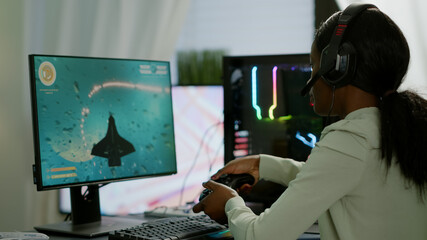 Pro african gamer playing online space shooter game on powerful computer using wireless controller...