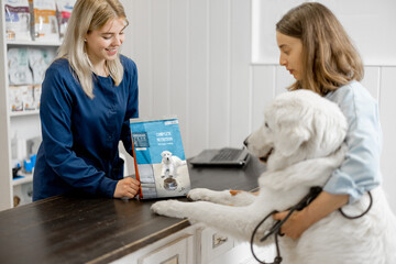 Female owner with big white dog on reception in veterinary clinic choosing dry food for the pet....