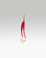 Minimal concept of jummy artisan white heart shaped chocolate with hot red bird eye chilli paper. Abstract modern arrangement against lovely gray background.