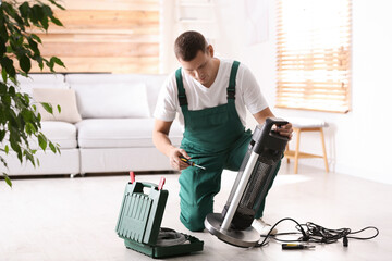 Professional technician repairing electric patio heater with screwdriver indoors