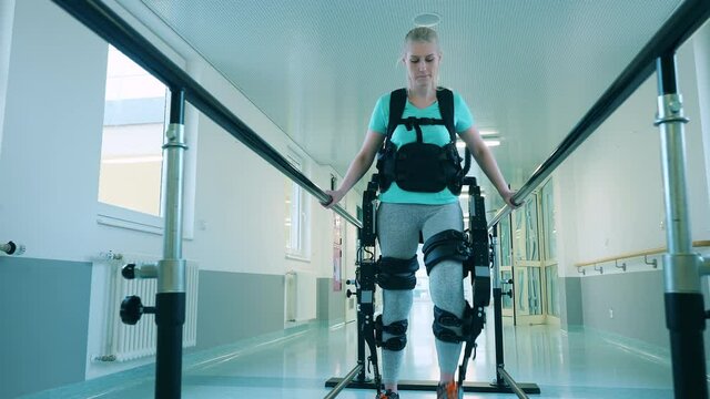 Female patient is wearing exoskeleton while walking practice