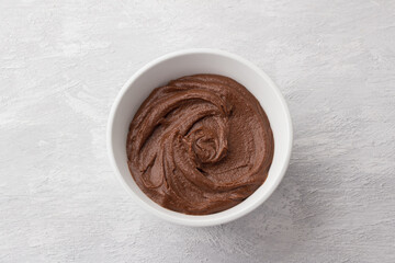 Delicious vegan chocolate nut spread in white bowl on light gray background