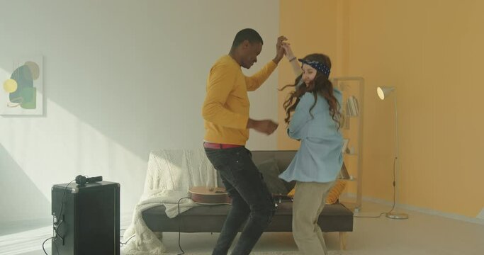 Multiracial dark skinned guy and white girl dancing jumping having fun smiling holding hands friends positive atmosphere at home