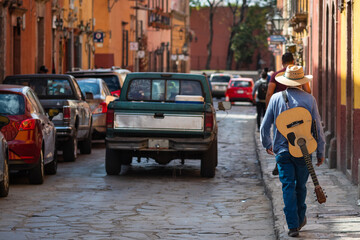 Street musician walking with his guitar on the streets of historical town San Miguel de Allende in Guanajuato, Mexico.