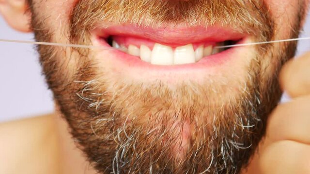 Close-up of the mouth of a bearded man cleaning his upper teeth with dental floss