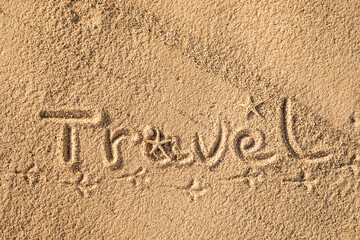 Word Travel written in the sand on the beach.  Summer travel concept. Birds footprints on yellow sand.