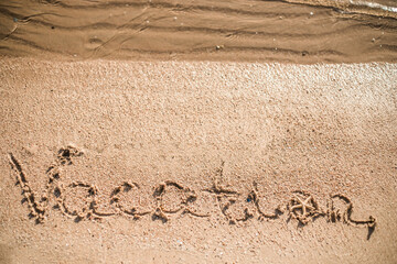 Word Vacation written in the sand on the beach.  Summer travel concept