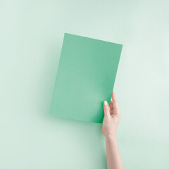 Minimal summer concept with hand holding a teal green paper card note on bright green background with copy space.  Sustainability and eco friendly layout with place for text message.