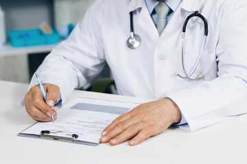 Confident old mature male doctor physician therapist working at office, handwriting notes. Close up wrinkled male doctor writing information in medical registration journal