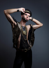 A gay young man in a vest and leather leggings on a gray background. Studio photo.