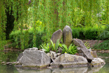 A stone island in the middle of the pond overgrown with ferns.
