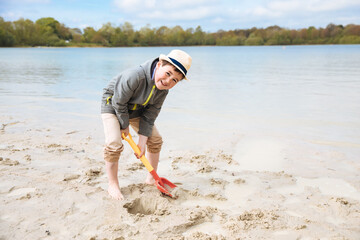 Child playing on the beach with a shovel. Child plays in the cold on the beach, in the sand 