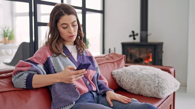 beautiful female using mobile chatting or watching photo in social media at home cozy house interior happy brunette sitting on the sofa happy weekend