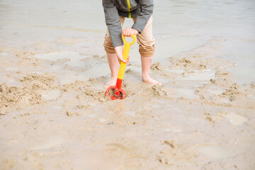 Child playing on the beach with a shovel. Child plays in the cold on the beach, in the sand 