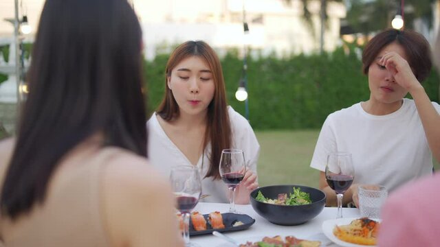 Happy Asian woman friends have dinner party in the garden together at night. Female friendship enjoy and having fun celebration party nightlife with eating food, drinking wine and talking together.