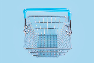 Top view of supermarket shopping basket on light blue background. Empty metal wire supermarket...