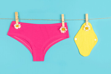 Yellow eco reusable menstrual pads and pink panties with chamomile flowers on washing line, blue...
