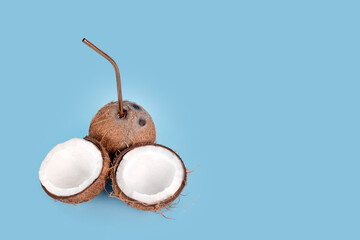 Open coconut with straw on blue background. Tropical drink, summer vacation minimal creative concept. Cracked coconut fruit with coconut milk inside, copy space for text