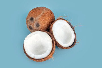 Whole and cracked coconuts on light blue background. De-husked coconut fruits showing the characteristic three pores. Cut in half coconut closeup.