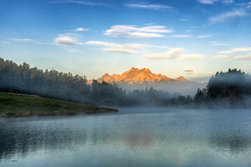 Fototapeta na wymiar Peaceful mountain scene with calm lake, colorful trees and high peaks in a golden warm light. Scenic view of High Tatras National Park, Slovakia.