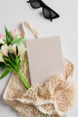 Summer fashion beige string bag with femenine accessories, bouquet of flowers, notebook Flat lay, top view.